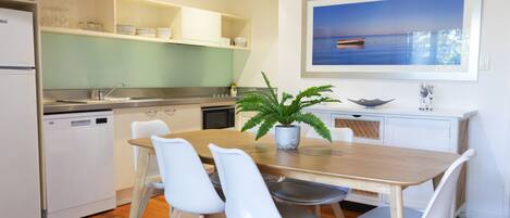 Une cuisine moderne avec des meubles blancs, une table à manger en bois et quatre chaises blanches.