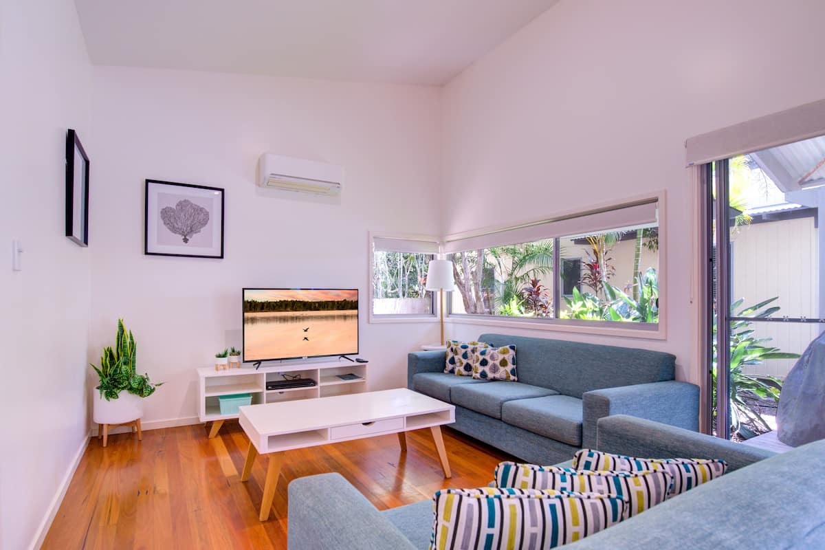 A modern living room with a flat-screen TV, a grey sofa, a coffee table, and a potted plant.