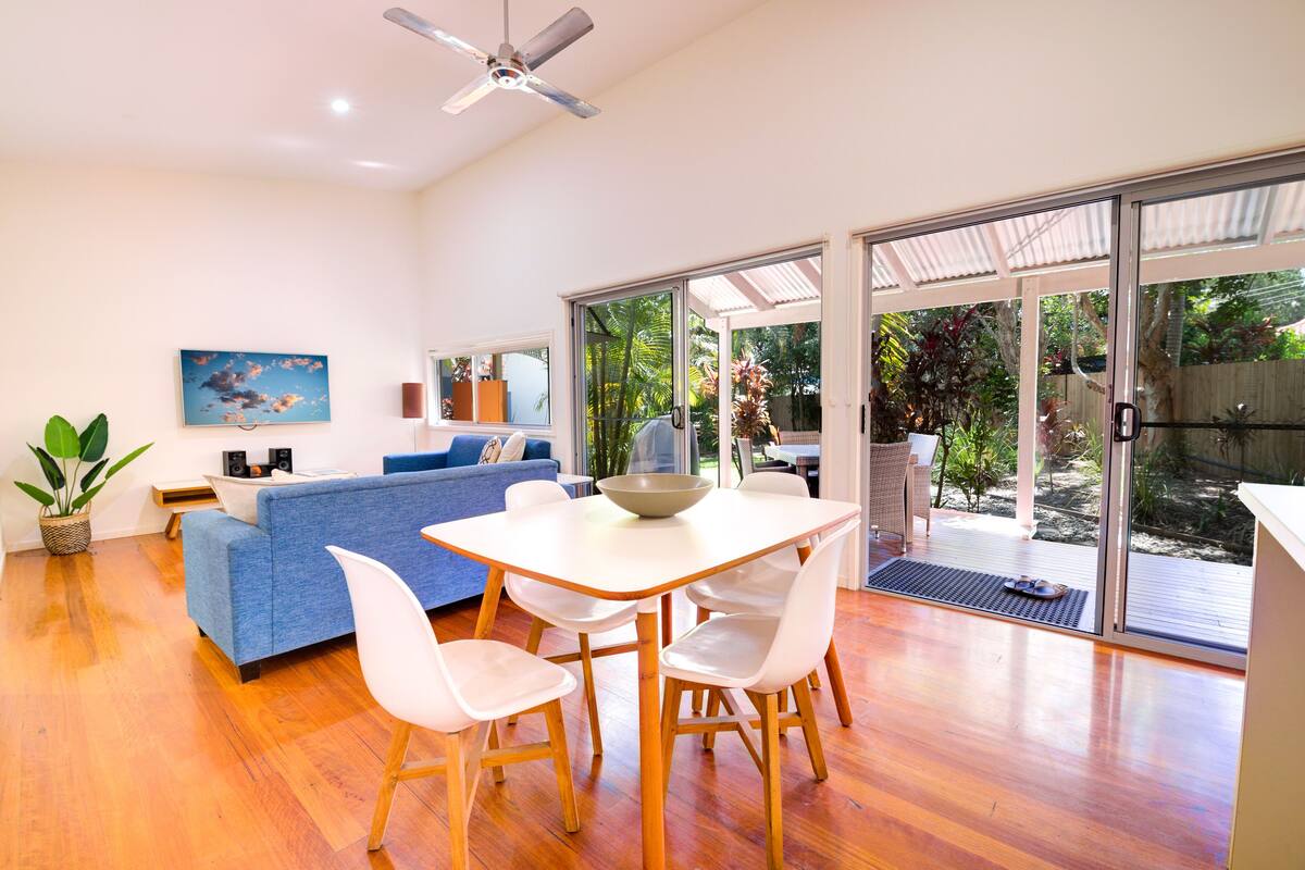 A modern living room with a dining area, large sliding glass doors to a backyard, and a ceiling fan.