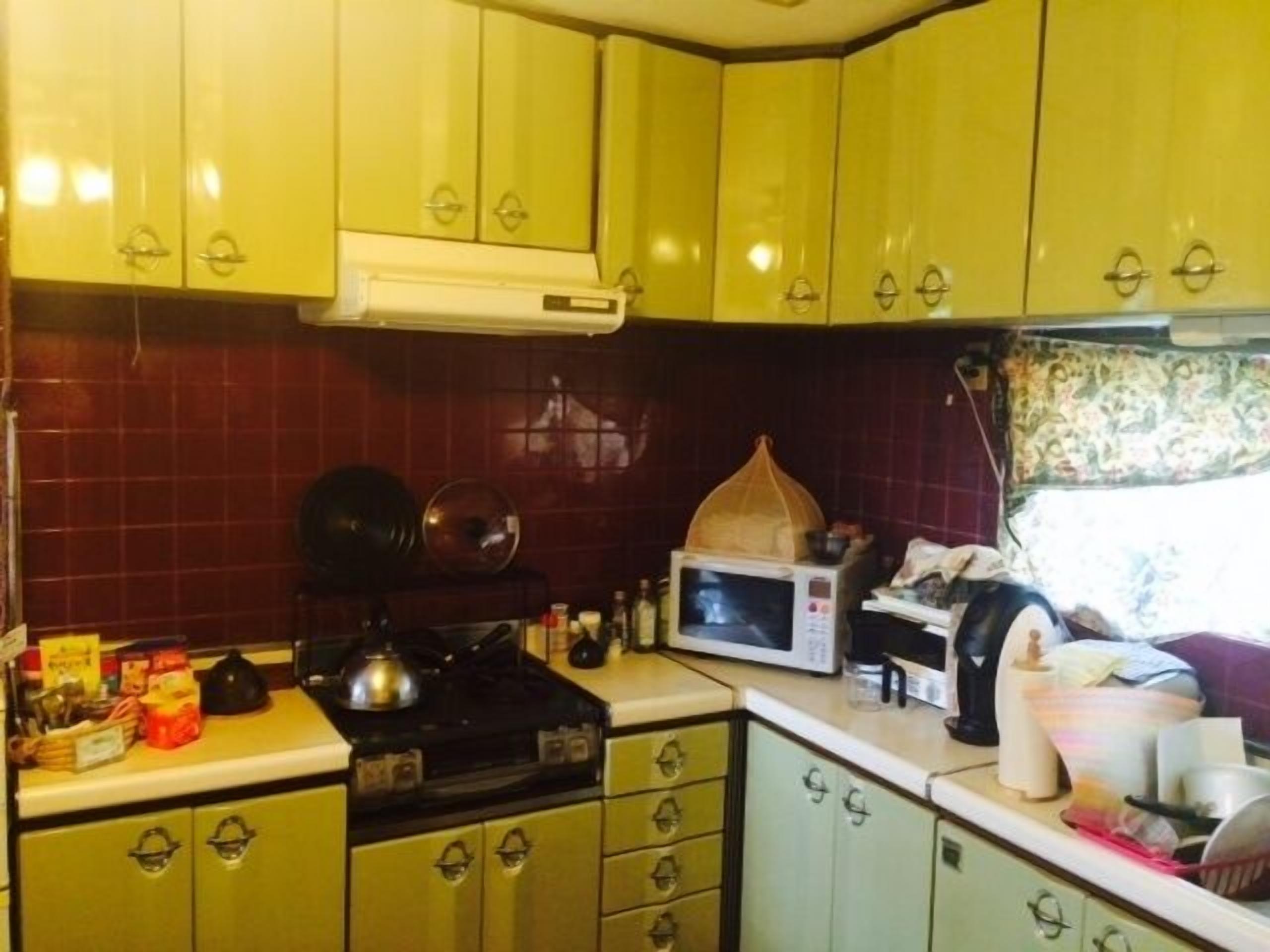 A kitchen with yellow cabinets, a stove, a microwave, and various kitchen items.
