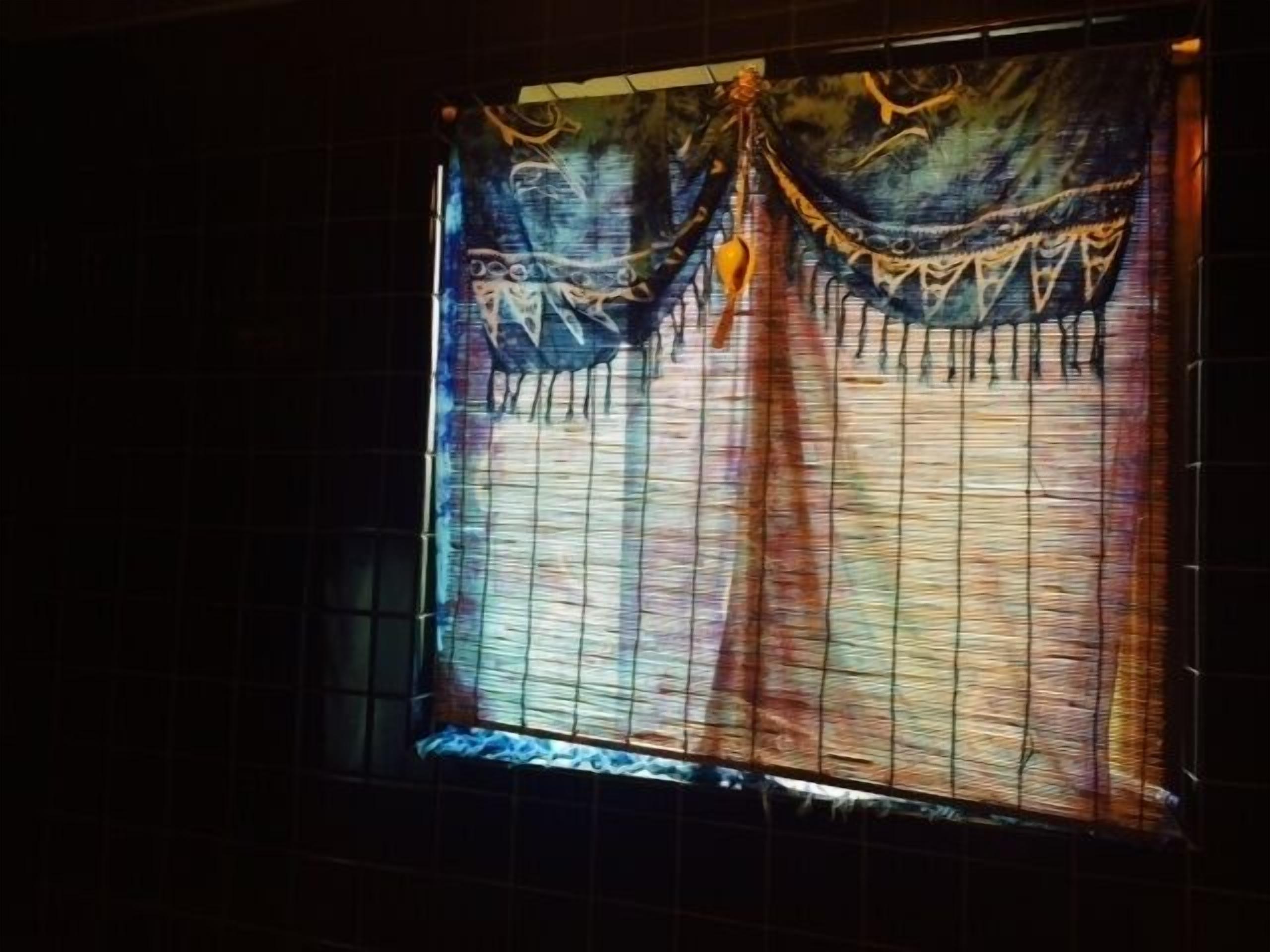 Una ventana con cortina estampada y un adorno colgando en la parte superior.
