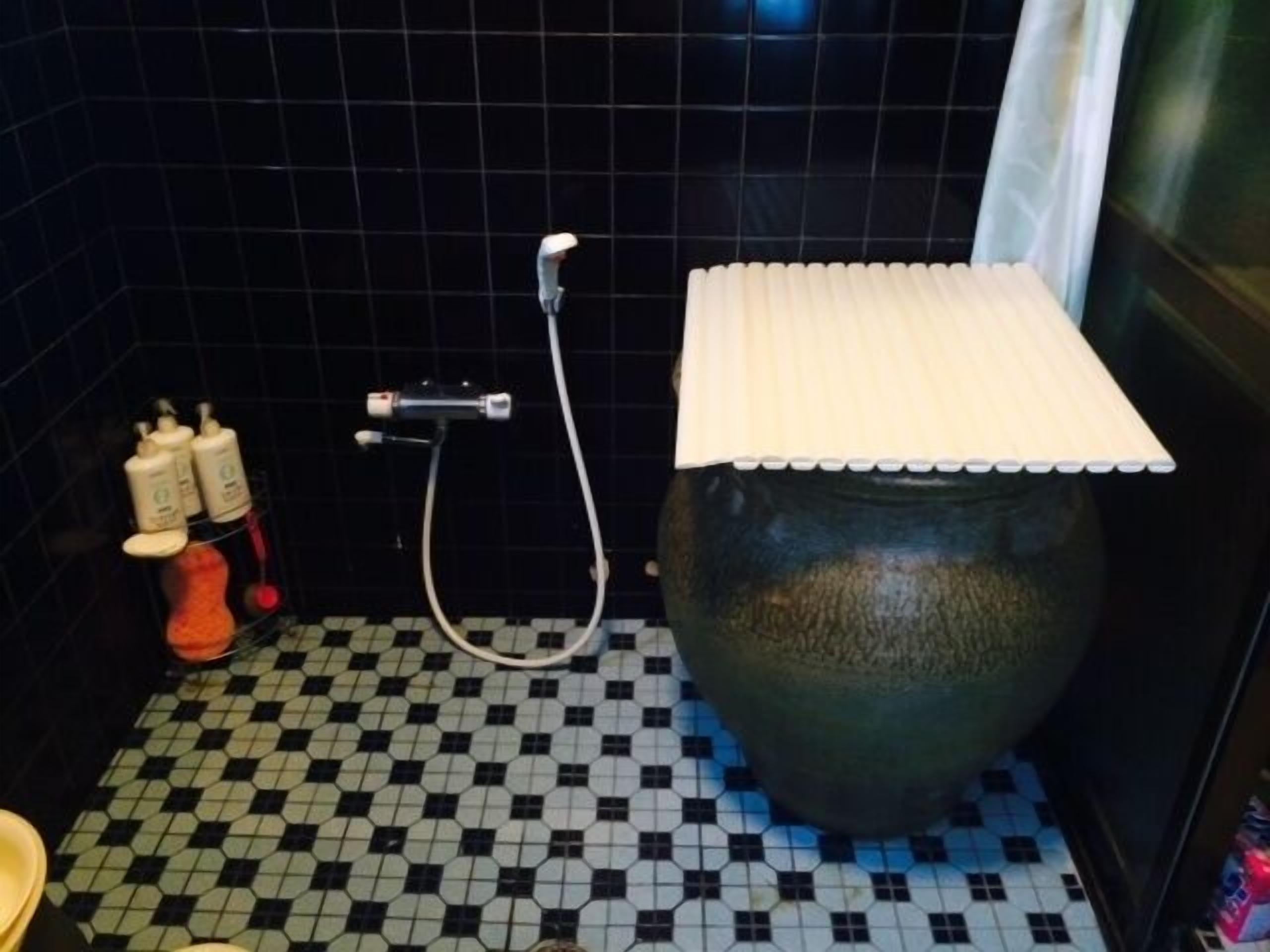 A bathroom with a tiled floor, a shower area with a hose, and a large vase.