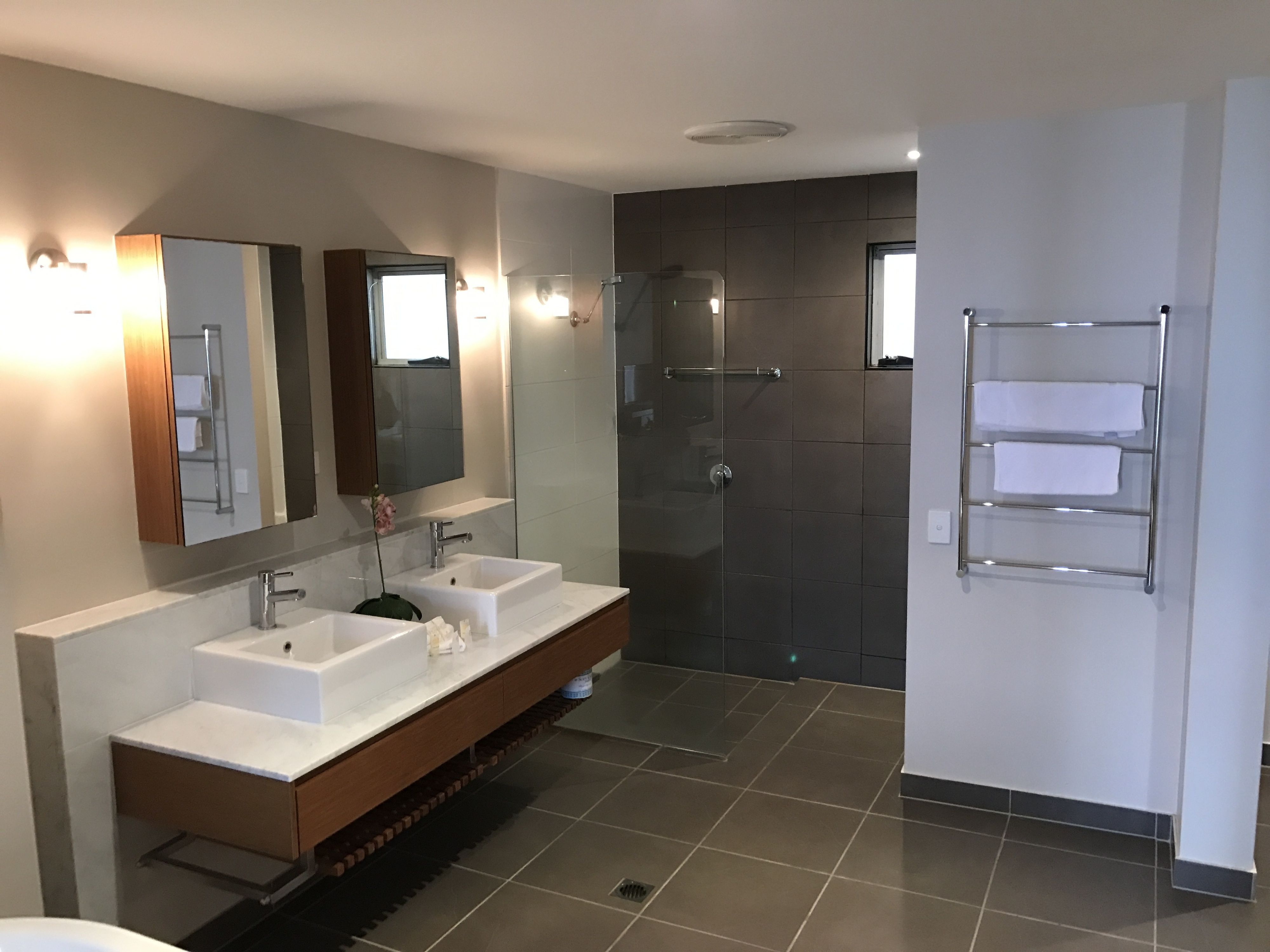 A modern bathroom with two sinks, a large mirror, a glass shower enclosure, and a towel rack.