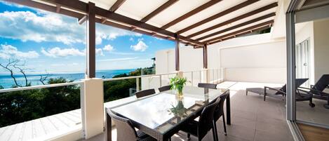 A balcony with a glass table and chairs, overlooking a scenic view.