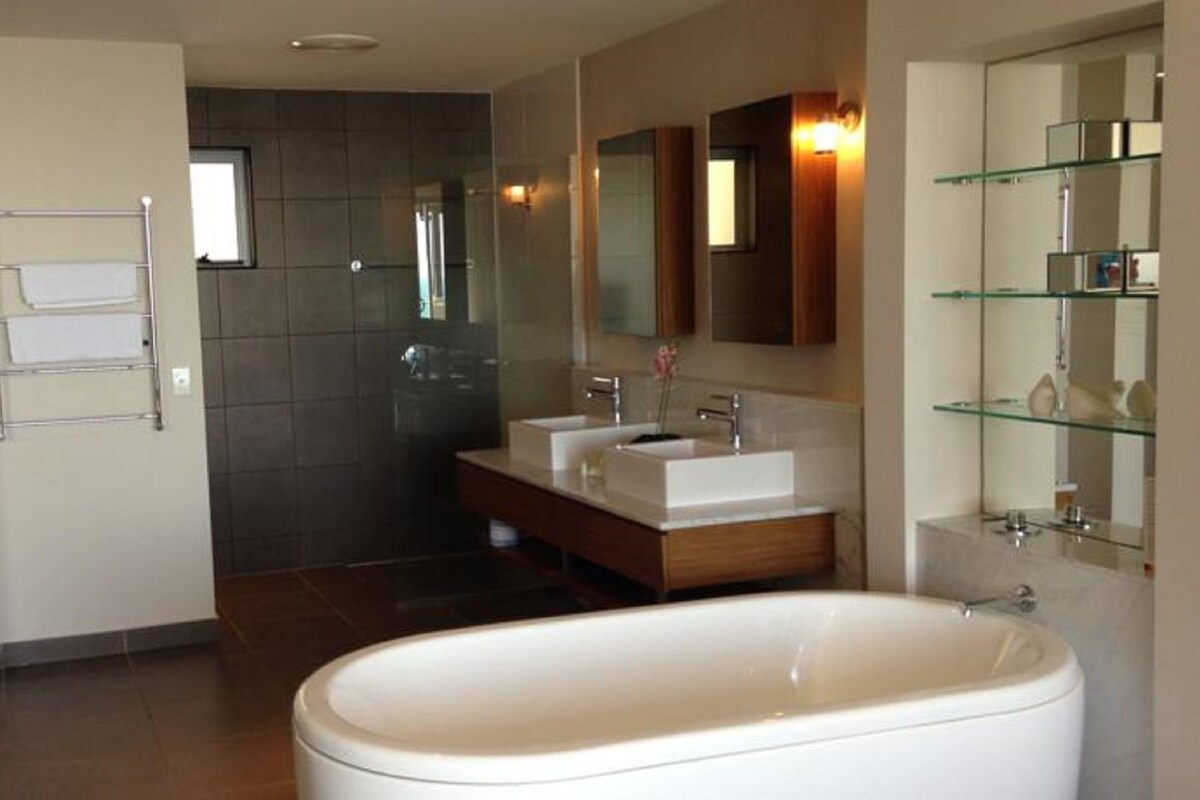 A modern bathroom with a freestanding bathtub, two sinks, and a glass shower enclosure.
