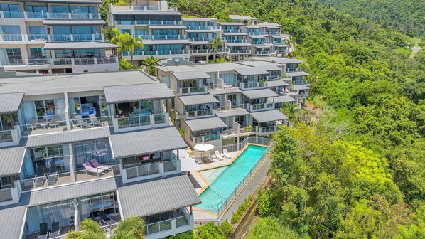 A modern resort with multiple two-story buildings, a central swimming pool, and lush surrounding greenery.