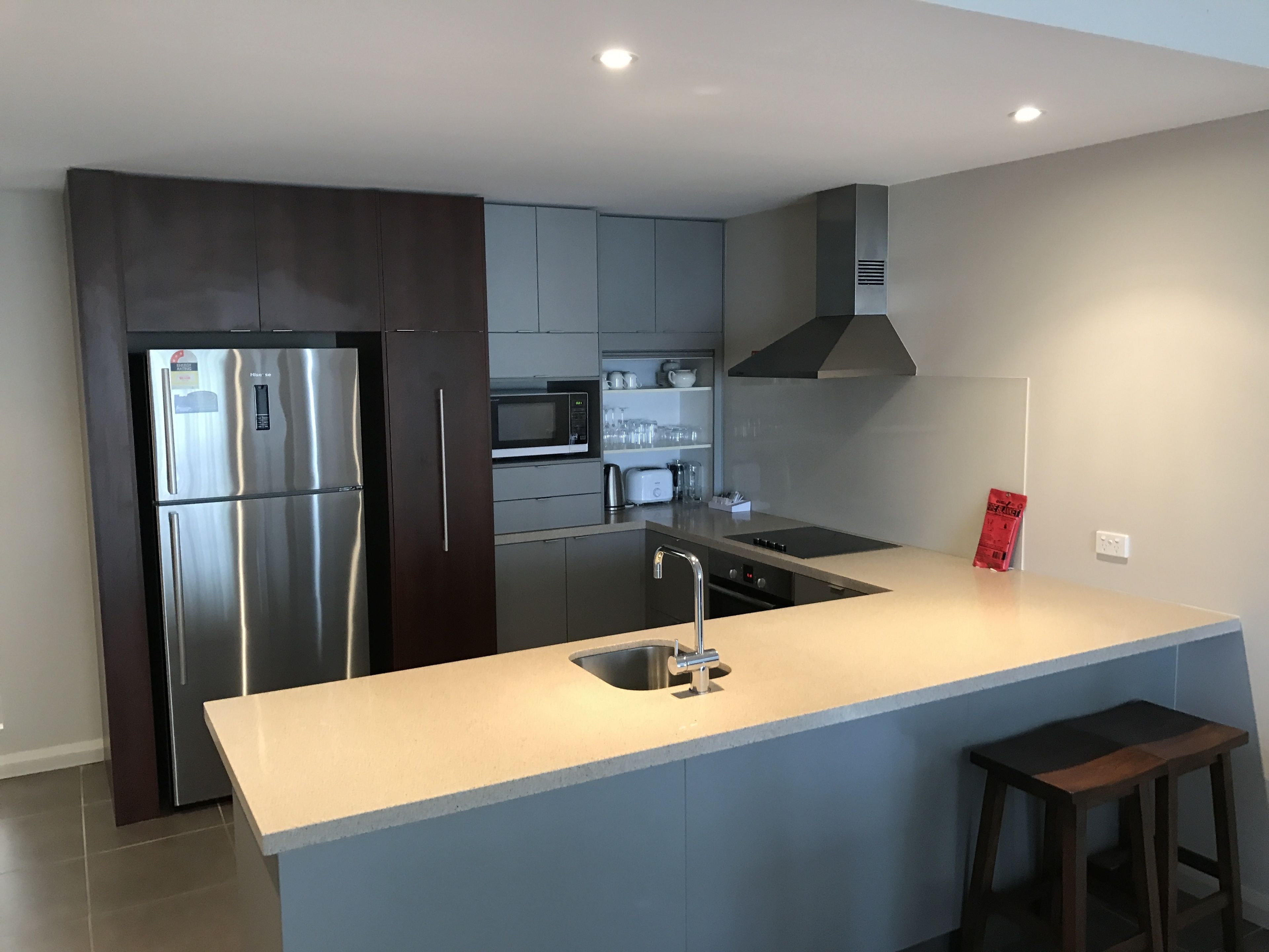 A modern kitchen with stainless steel appliances, grey cabinetry, and a central island with a sink.
