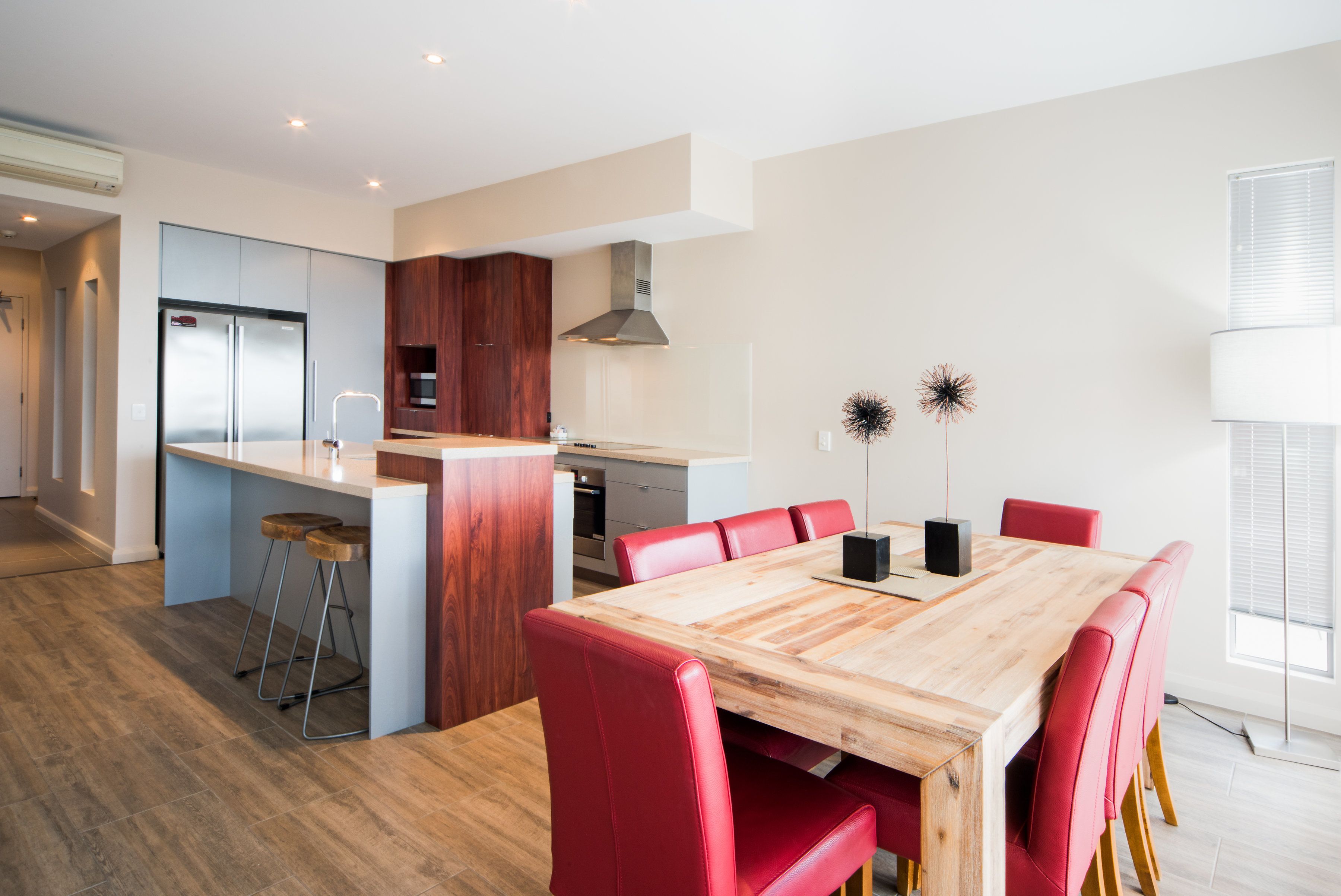 Una cocina moderna con una isla integrada, sillas rojas y una mesa de comedor de madera.