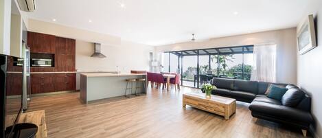 A modern living room with a black leather sofa, wooden coffee table, and a dining area with red chairs.