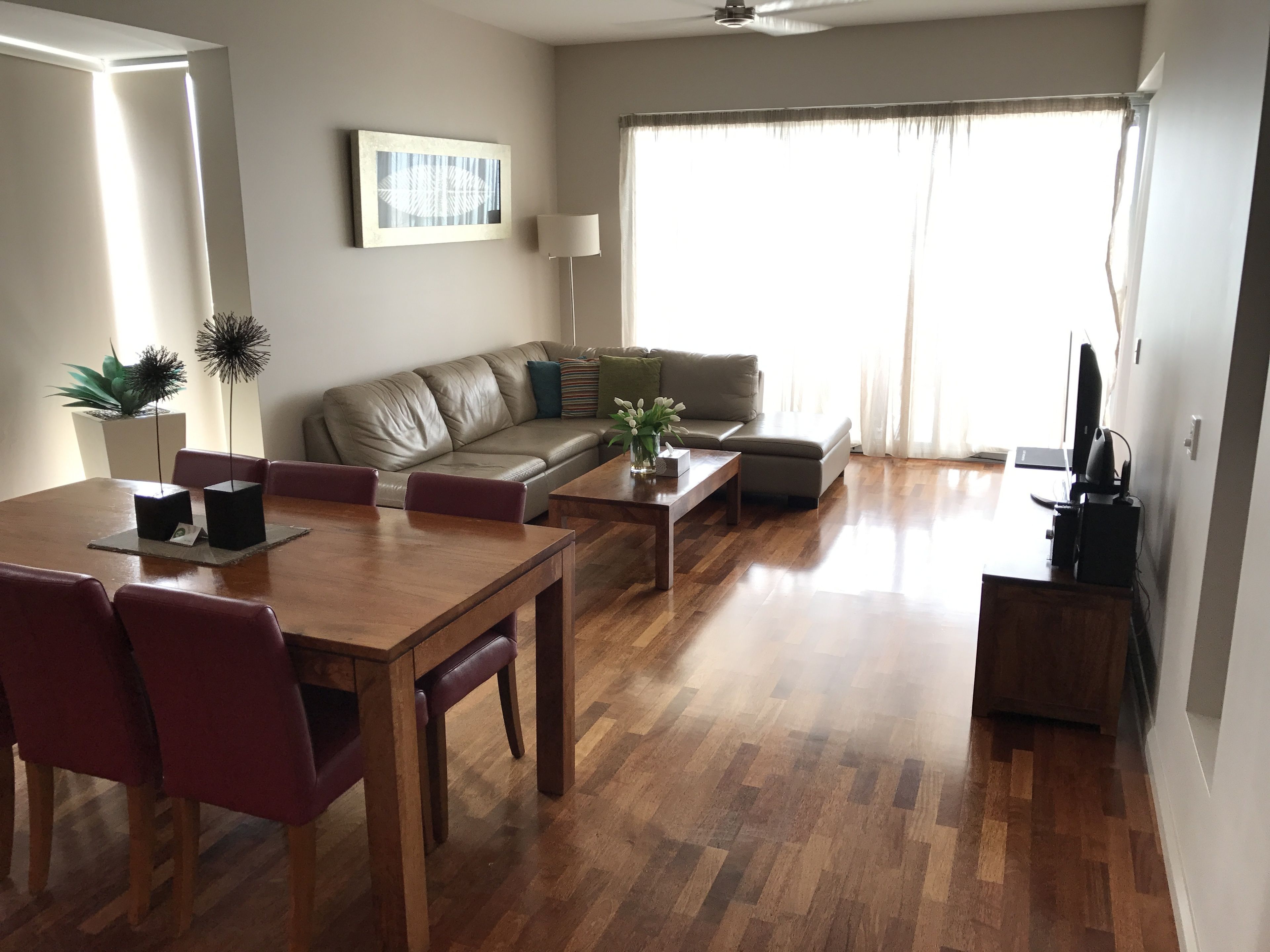 Uma sala de estar moderna com uma mesa de jantar de madeira, sofá de couro e uma televisão.