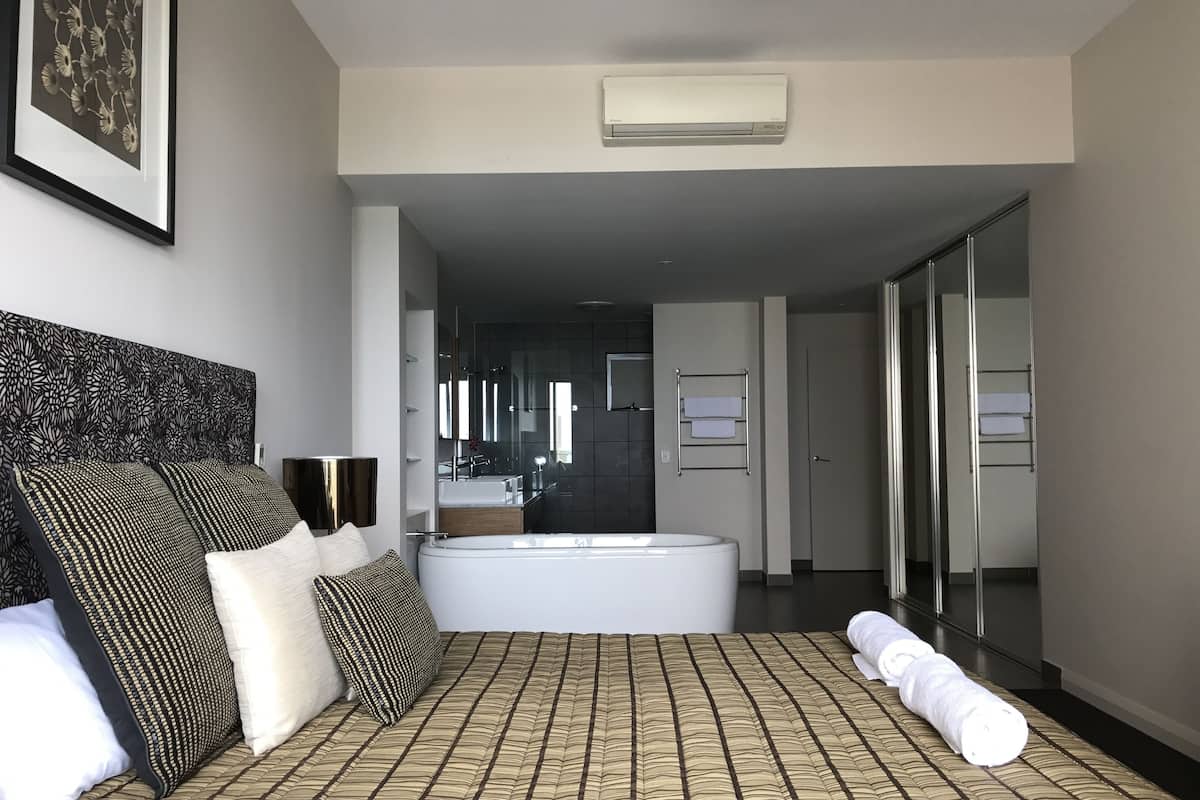 Une chambre d’hôtel moderne avec un grand lit, une baignoire et un dressing.