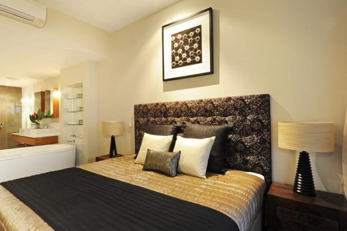 Une chambre d’hôtel avec un grand lit, une table de chevet avec une lampe, une salle de bain avec une baignoire et une œuvre d’art encadrée au mur.