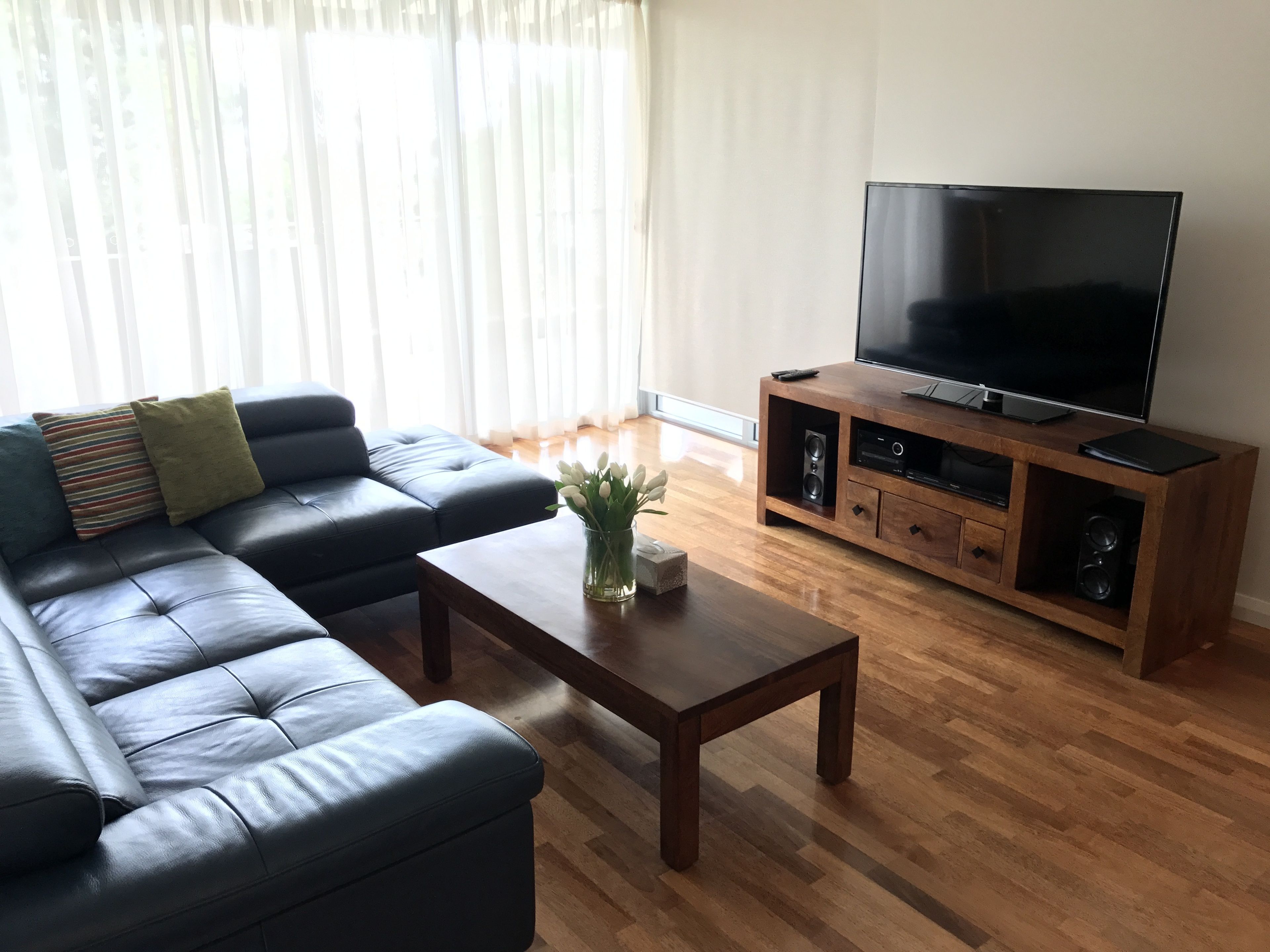 A living room with a black leather sofa, a wooden coffee table, and a TV on a wooden stand.