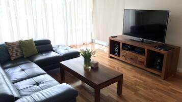 A living room with a black leather sofa, a wooden coffee table, and a TV on a wooden stand.