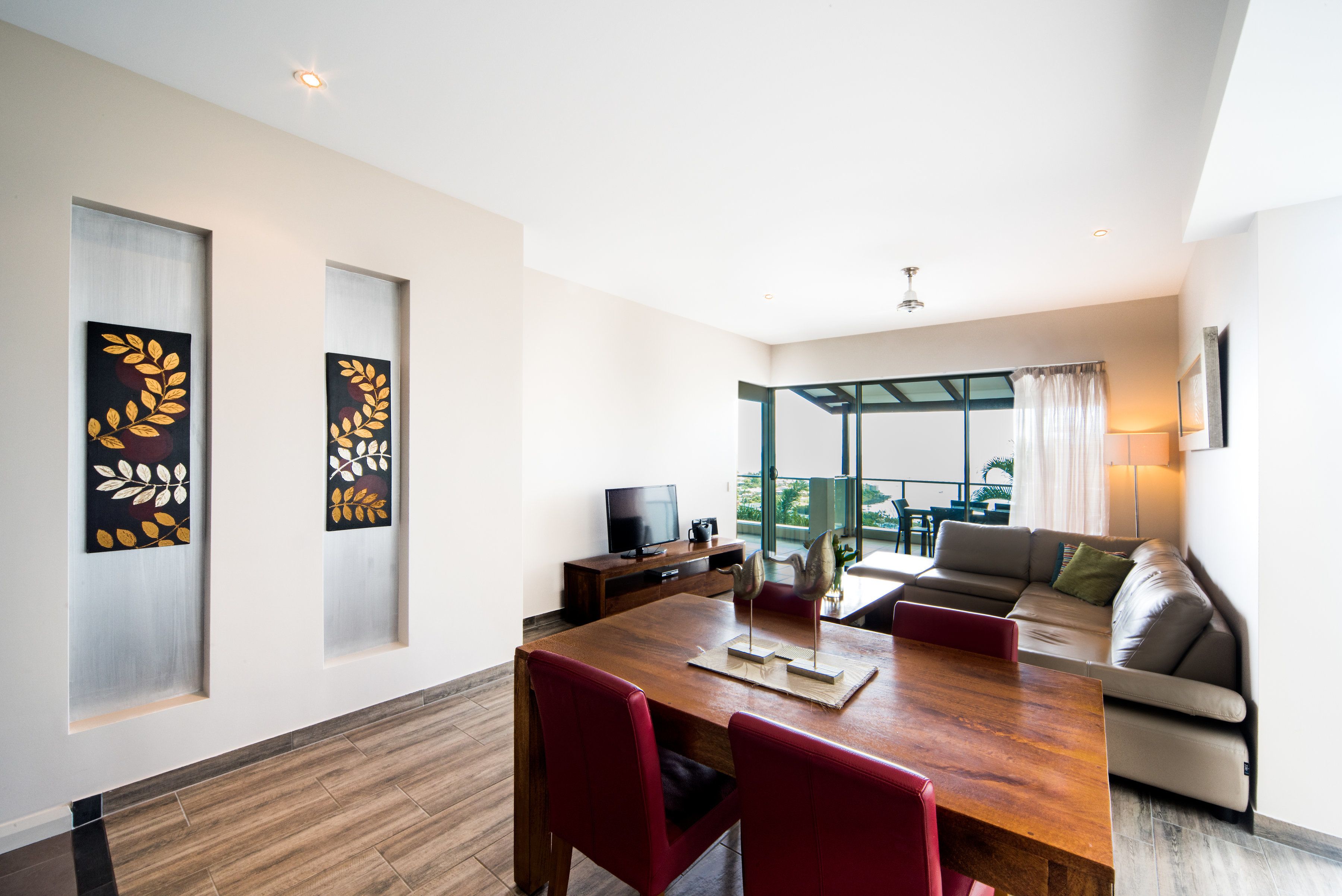 A modern living room with a wooden dining table, red chairs, a sofa, and a television.