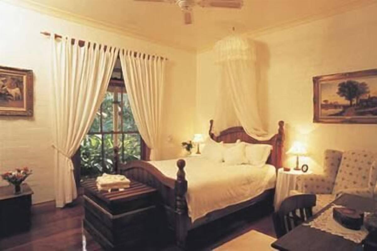 A bedroom with a bed, a nightstand, a chair, and a window with curtains.