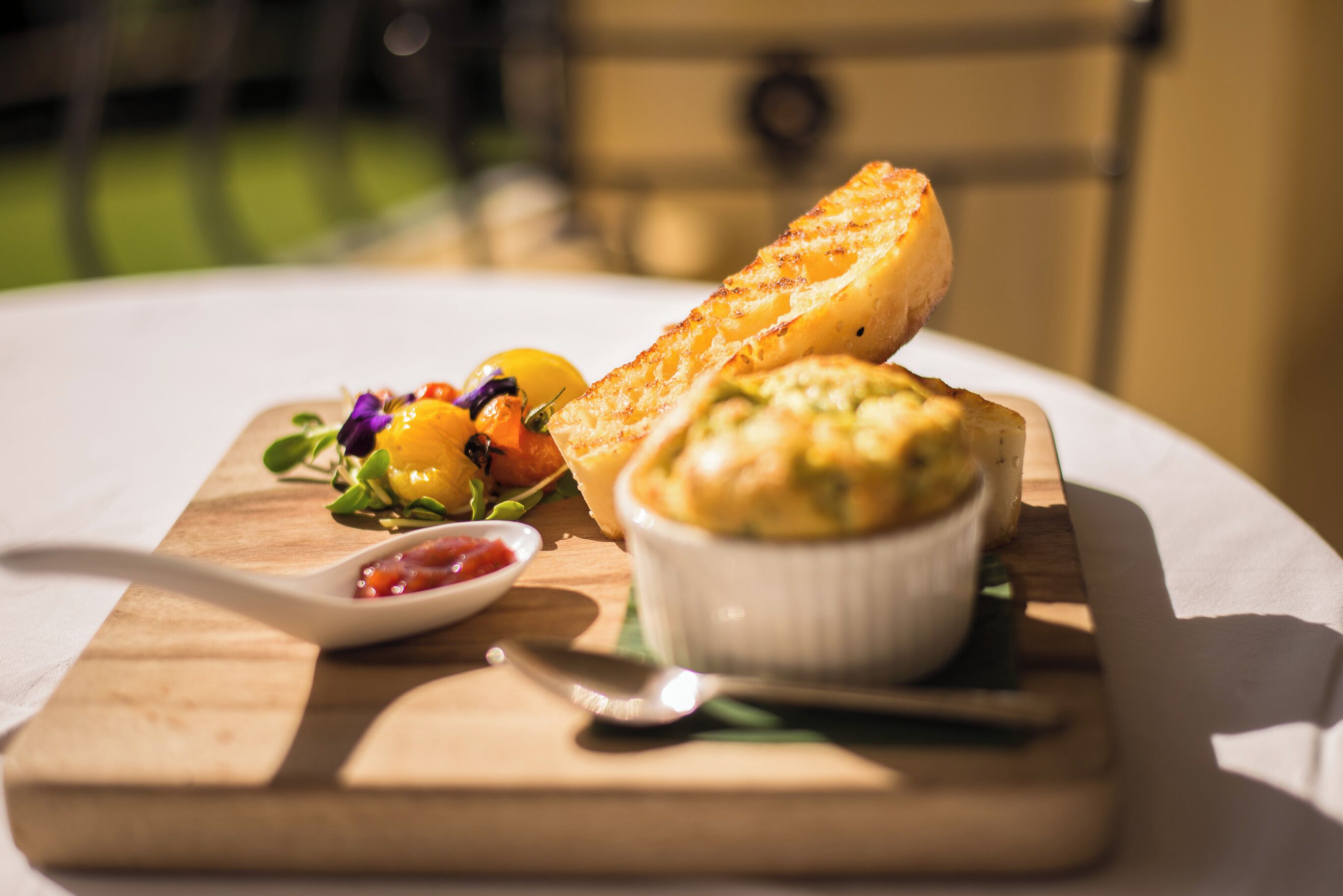 Une planche en bois sur laquelle on a disposé un sandwich au fromage grillé, un bol de soupe et une petite assiette de confiture, le tout sur une nappe blanche.
