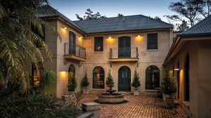 A two-story building with a courtyard, featuring a fountain, potted plants, and a brick pathway. - Abbie's Byron Bay Villa (Ewingsdale)