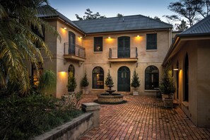 A two-story building with a courtyard, featuring a fountain, potted plants, and a brick pathway.