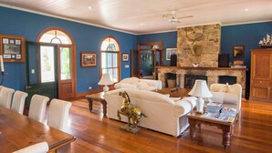 A spacious living room with a fireplace, a dining table, and a large window. - Abbie's Byron Bay Villa (Ewingsdale)