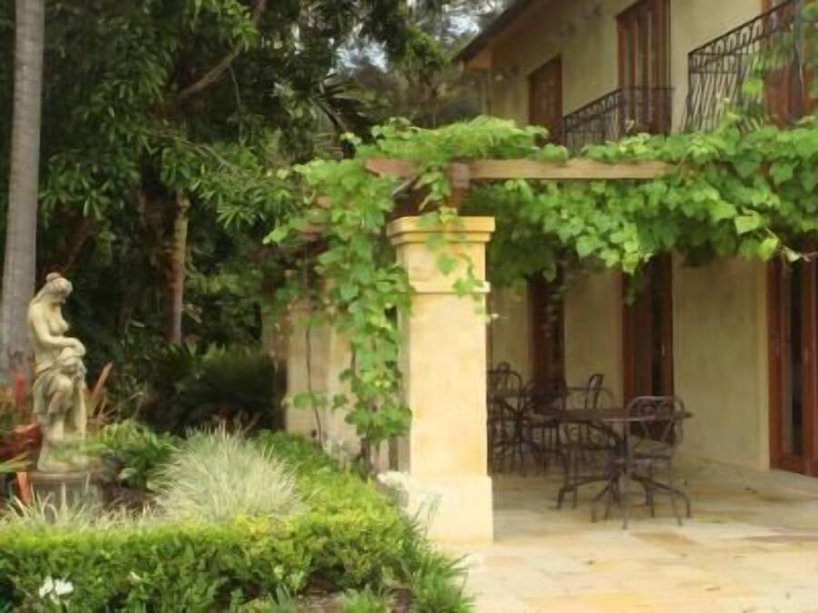Un patio con una estatua, una pérgola cubierta de hiedra y un edificio con balcón.