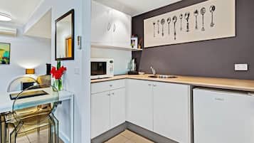 Una cocina moderna con armarios blancos, microondas, fregadero y refrigerador. Cuenta con un comedor con mesa de vidrio y sillas, y un jarrón con flores rojas.
