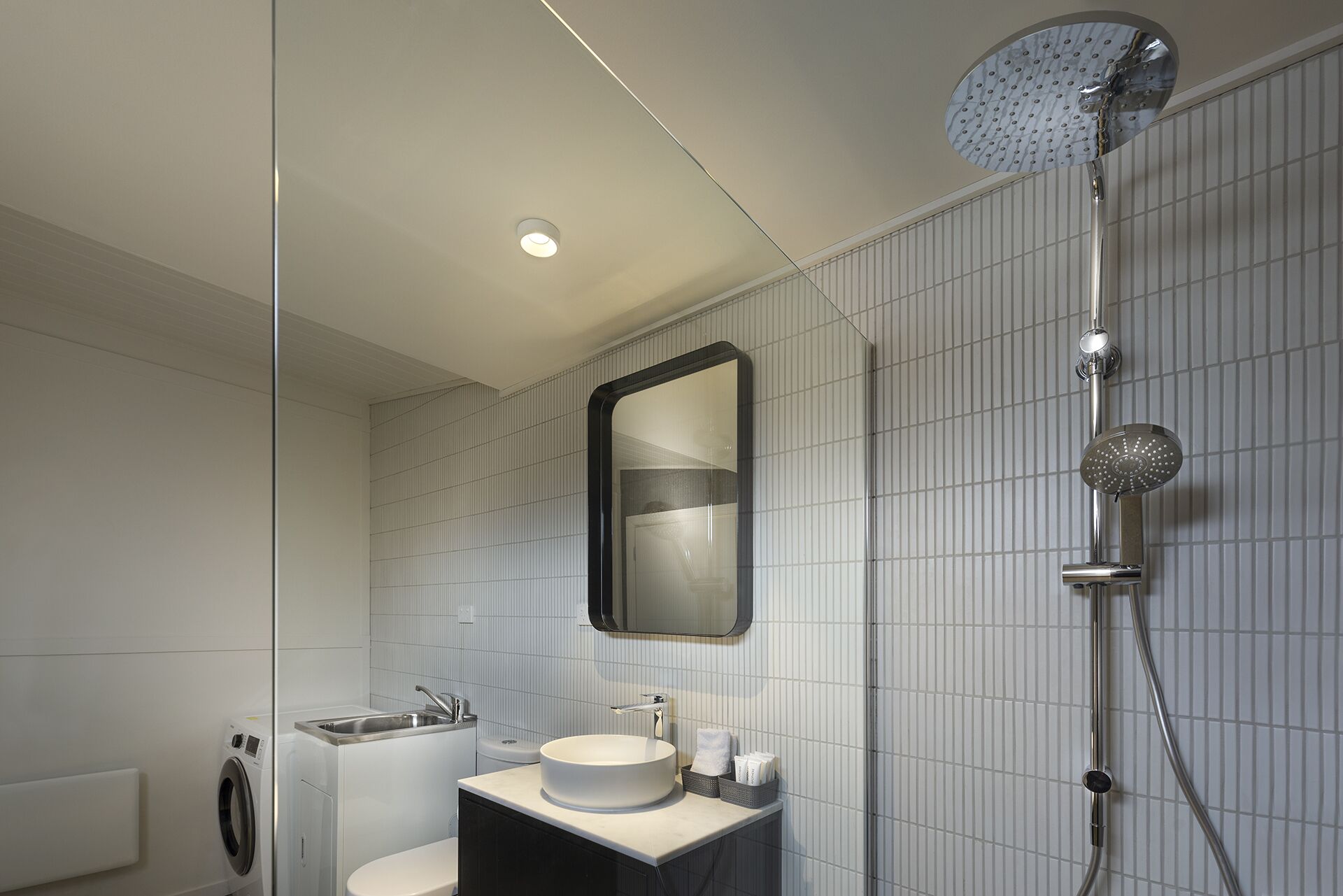 Un baño moderno con un espejo redondo, un lavabo, un inodoro y una ducha.