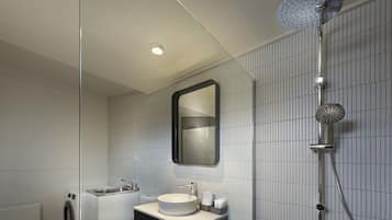Un baño moderno con un espejo redondo, un lavabo, un inodoro y una ducha.