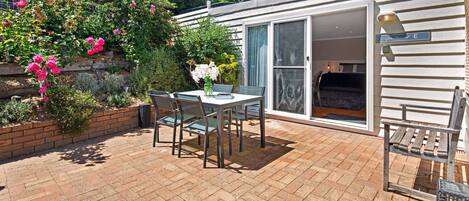 Une terrasse avec une table et des chaises, entourée d’un mur de briques et d’une végétation luxuriante.