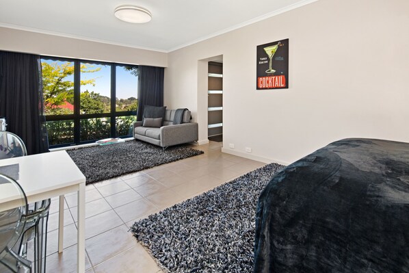 A modern hotel room with a large window, a grey sofa, a black bed, and a small table. - Daylesford Spa Accommodation (Daylesford)