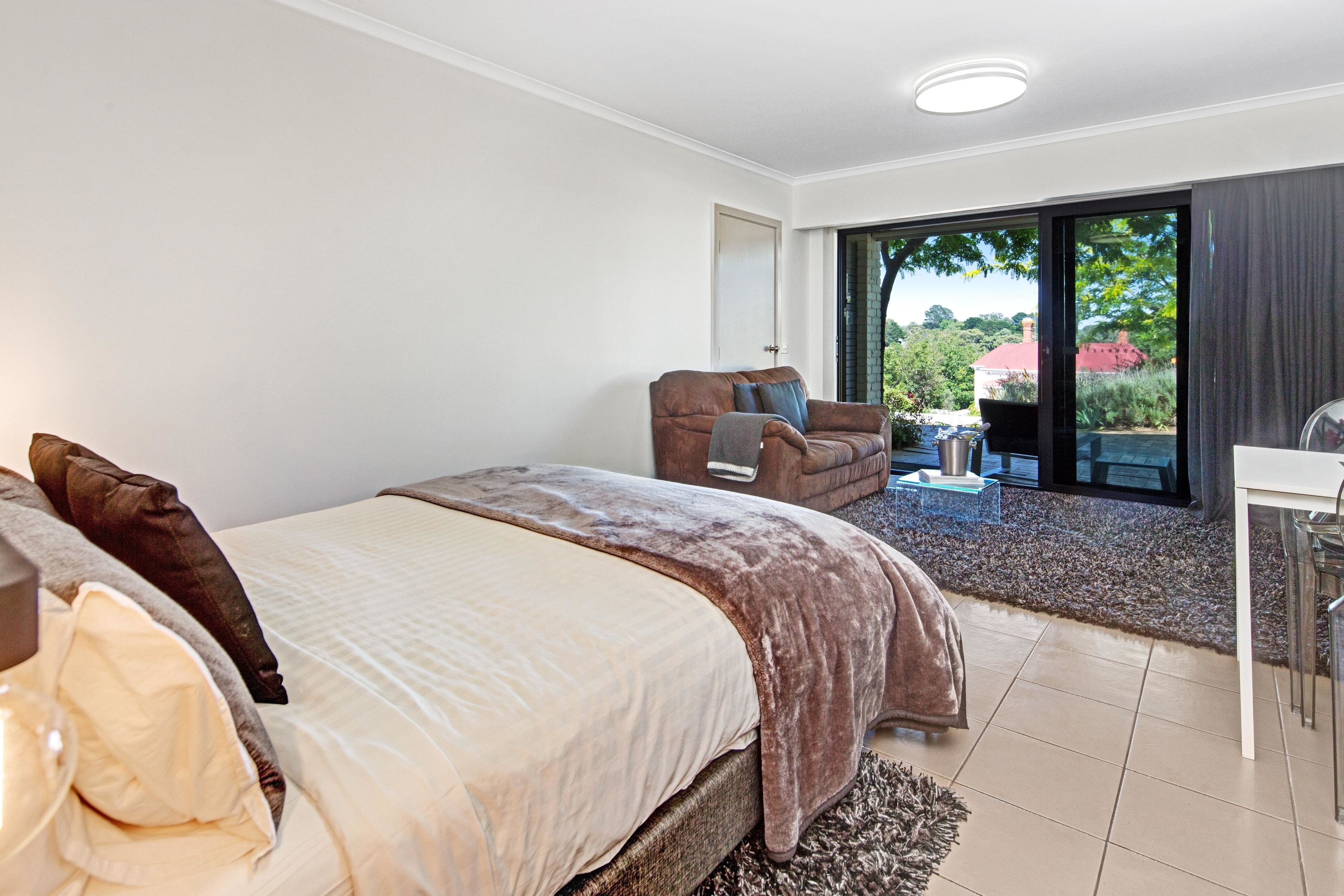 A bedroom with a bed, a chair, a table, and a sliding glass door leading to an outdoor area.
