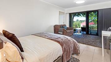A bedroom with a bed, a chair, a table, and a sliding glass door leading to an outdoor area.