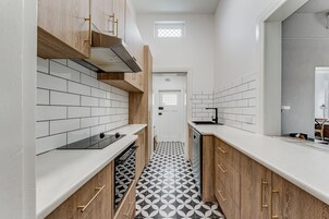 Una cocina estrecha con azulejos blancos tipo metro, armarios de madera y piso con estampado blanco y negro.