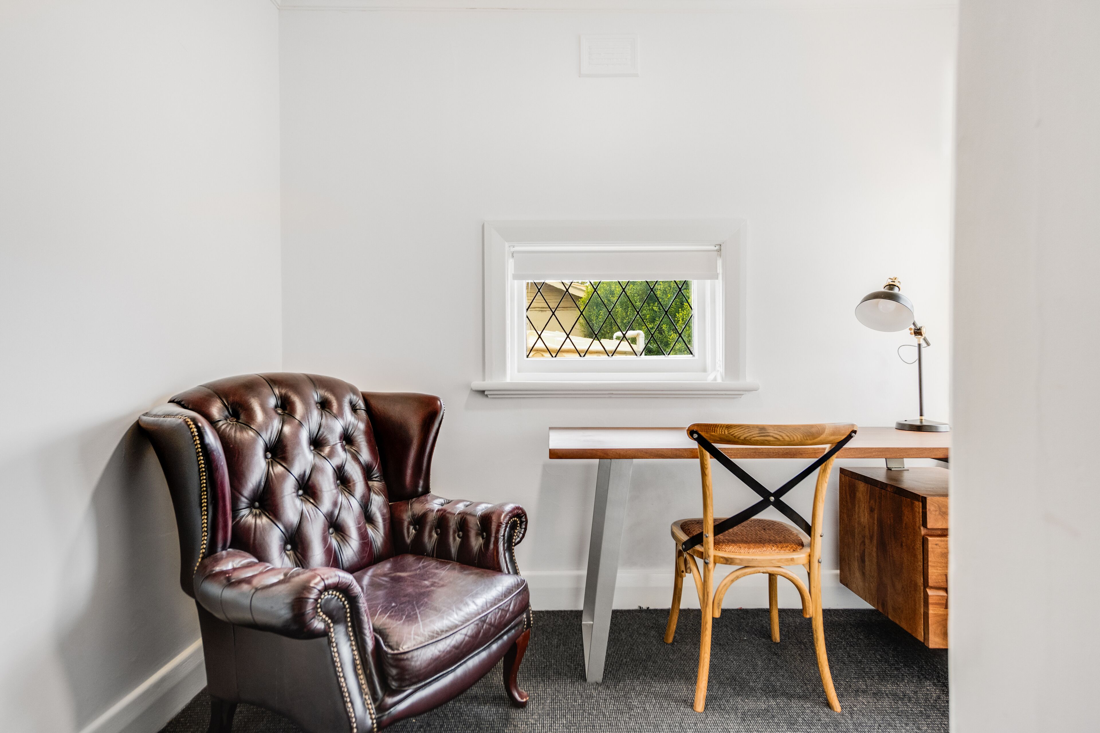 Une pièce comprenant un fauteuil en cuir, une chaise en bois, un bureau et une lampe.
