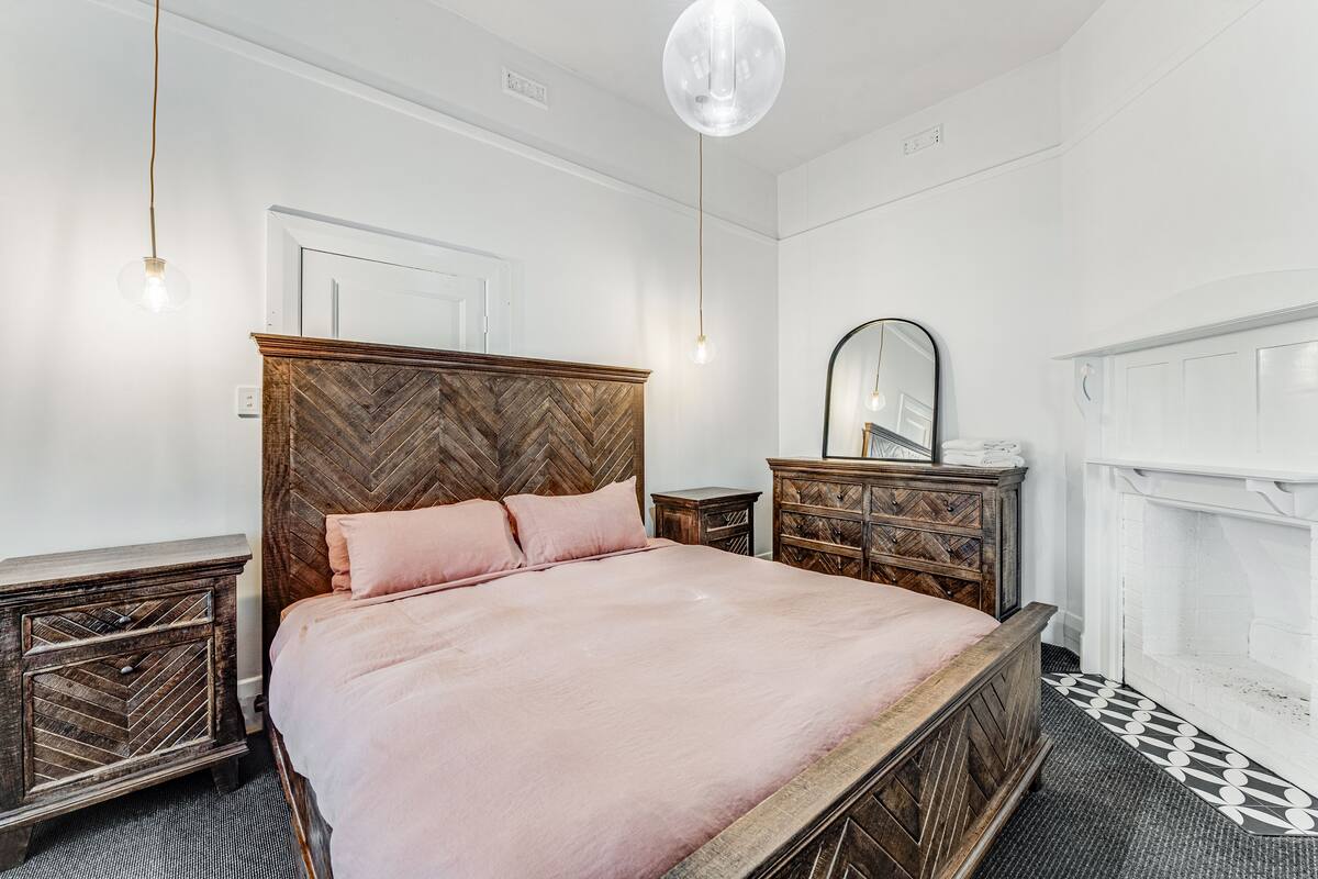 A bedroom with a herringbone-patterned headboard, a wooden nightstand, a dresser, and a mirror.