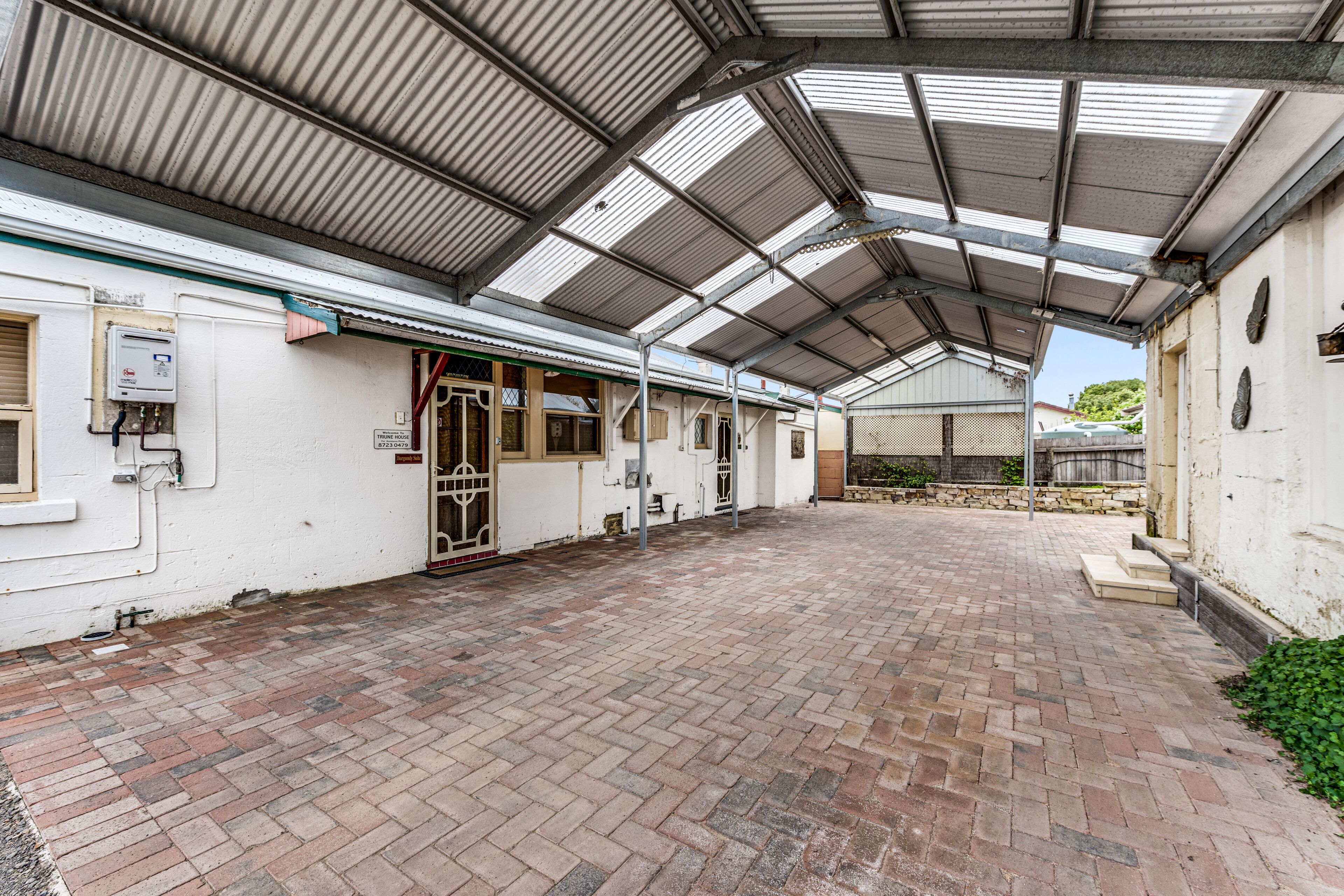 A covered outdoor area with a brick floor, metal roof, and white walls.