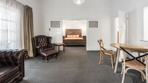 A hotel room with a large bed, a leather sofa, a wooden dining table, and a chandelier. - Wyatt Guest House (Mount Gambier)