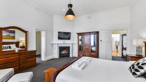 A hotel room with a large bed, a wooden dresser, a mirror, a television, and a fireplace. - Wyatt Guest House (Mount Gambier)