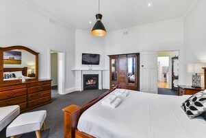Una habitación de hotel con una cama grande, un aparador de madera, un espejo, un televisor y una chimenea.