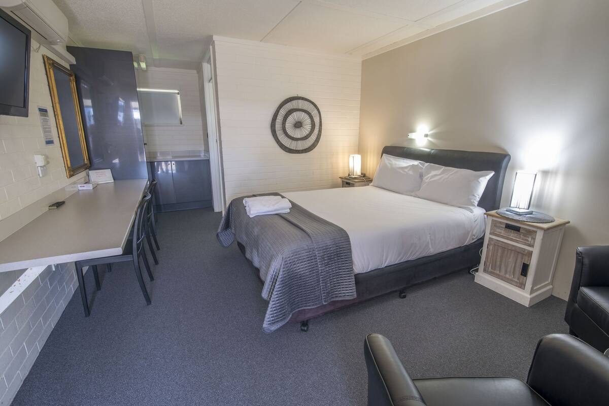 Ein Hotelzimmer mit Bett, Nachttisch, Lampe und einem kleinen Schreibtisch mit Stühlen.
