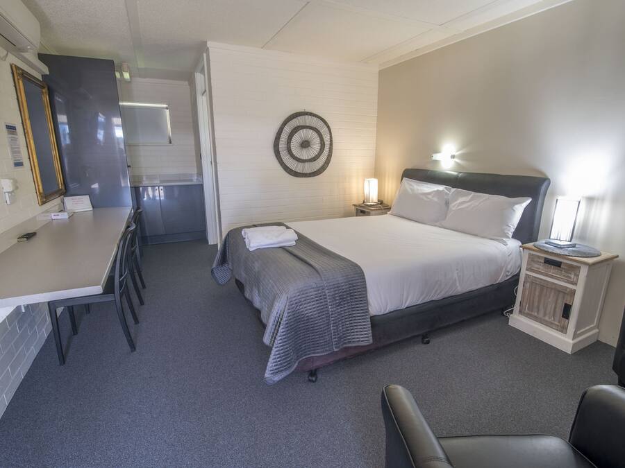 Habitación de hotel con cama, mesita de noche, lámpara y un pequeño escritorio con sillas.
