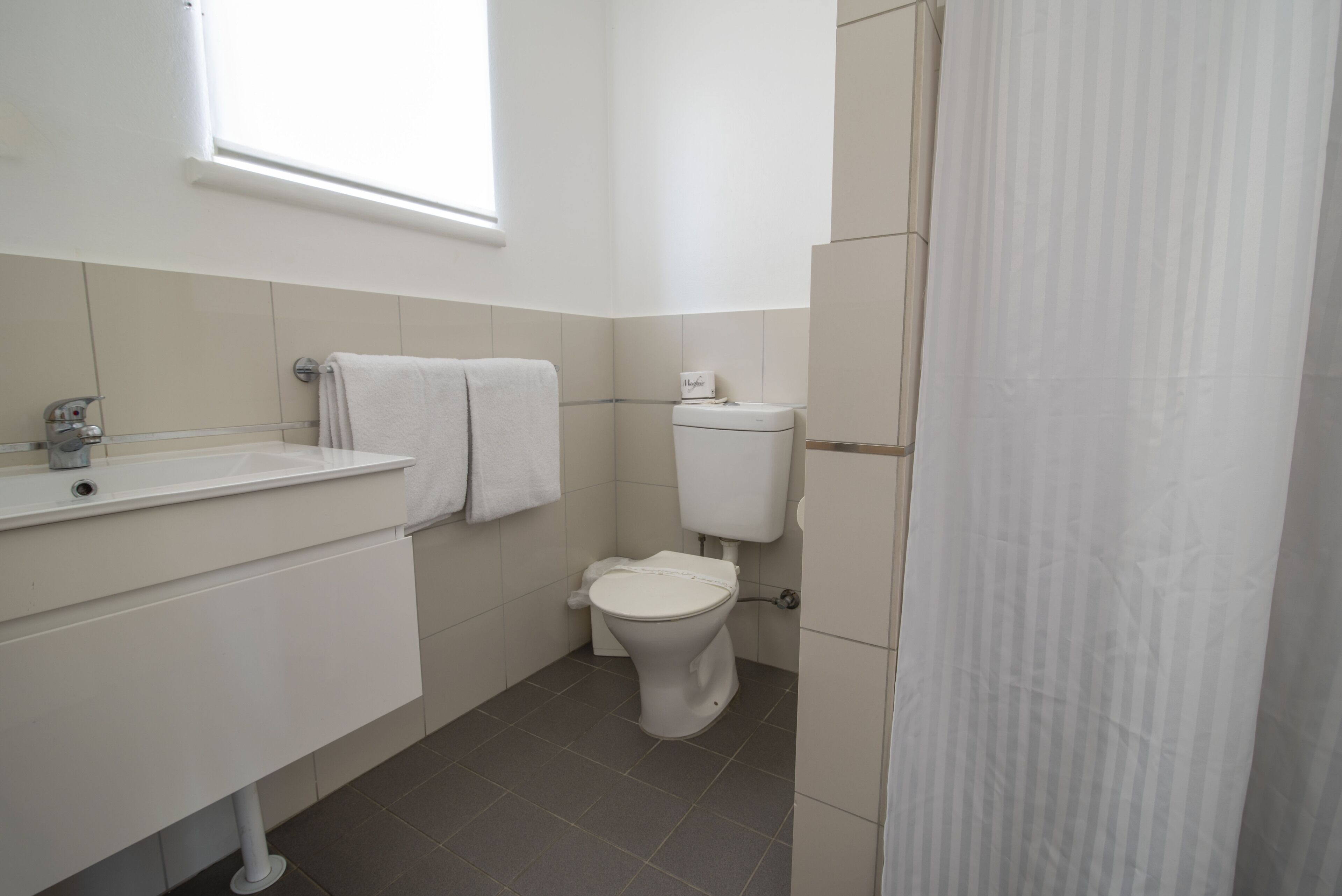 A small, clean bathroom with a toilet, sink, and a window providing natural light.