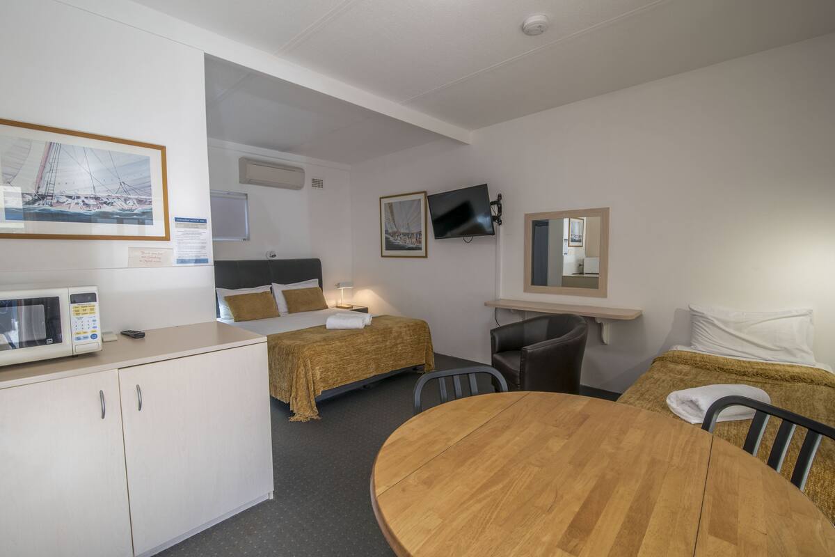 Ein Zimmer mit einem Bett, einem Schreibtisch, einem Stuhl, einem Tisch, einem Fernseher und einer Mikrowelle.