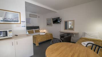 Una habitación con cama, escritorio, silla, mesa, televisor y microondas.