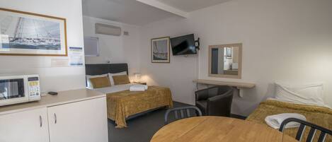 A room with a bed, a desk, a chair, a table, a TV, and a microwave.
