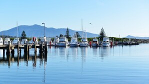 A marina with boats docked, calm water, and a mountain in the background. - Bermagui Motor Inn (Bermagui)