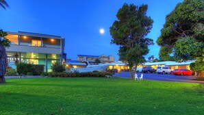 A modern hotel with a well-maintained lawn, a parking area, and a visible boat dock. - Bermagui Motor Inn (Bermagui)