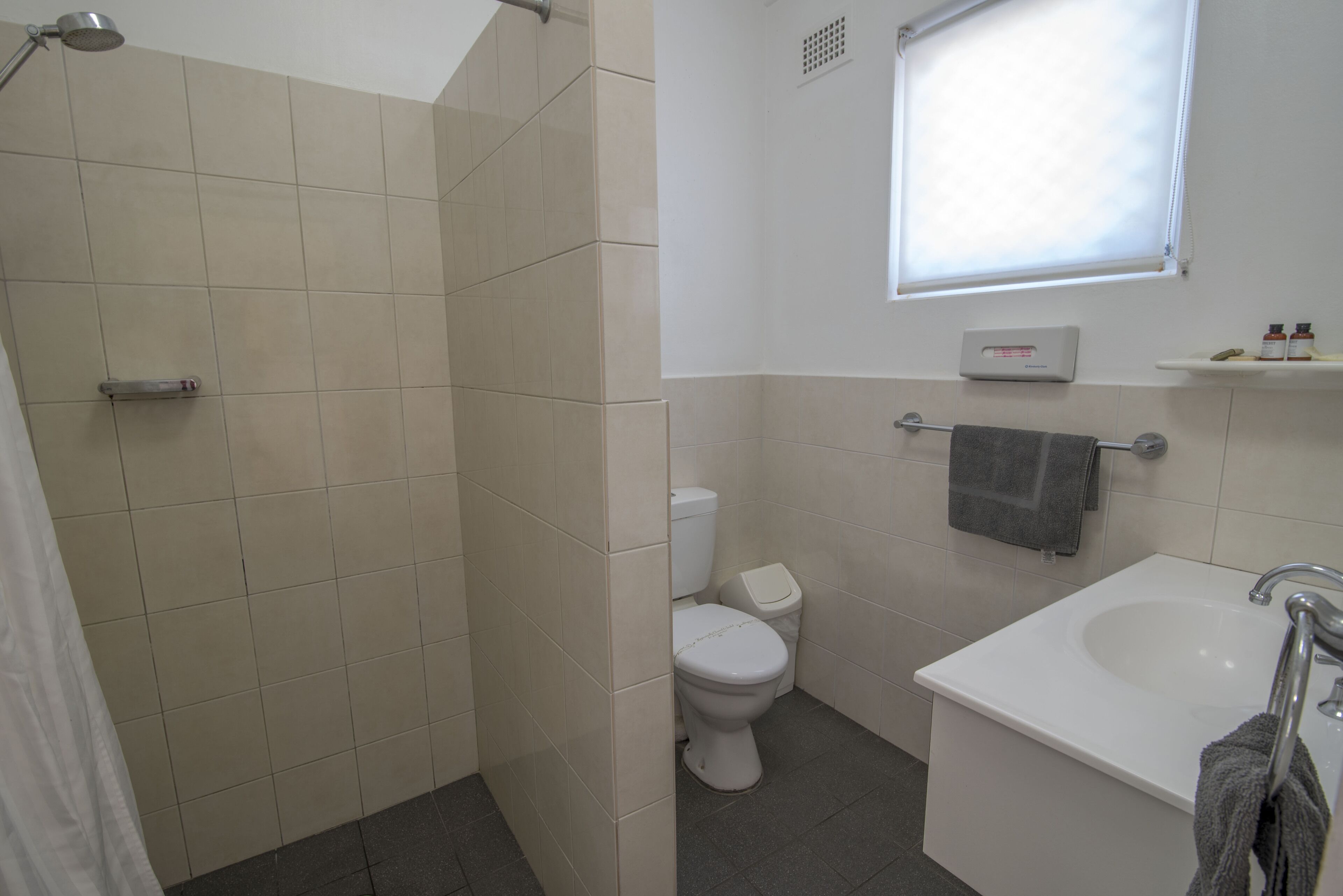 A bathroom with a shower, toilet, sink, and a window above the sink.