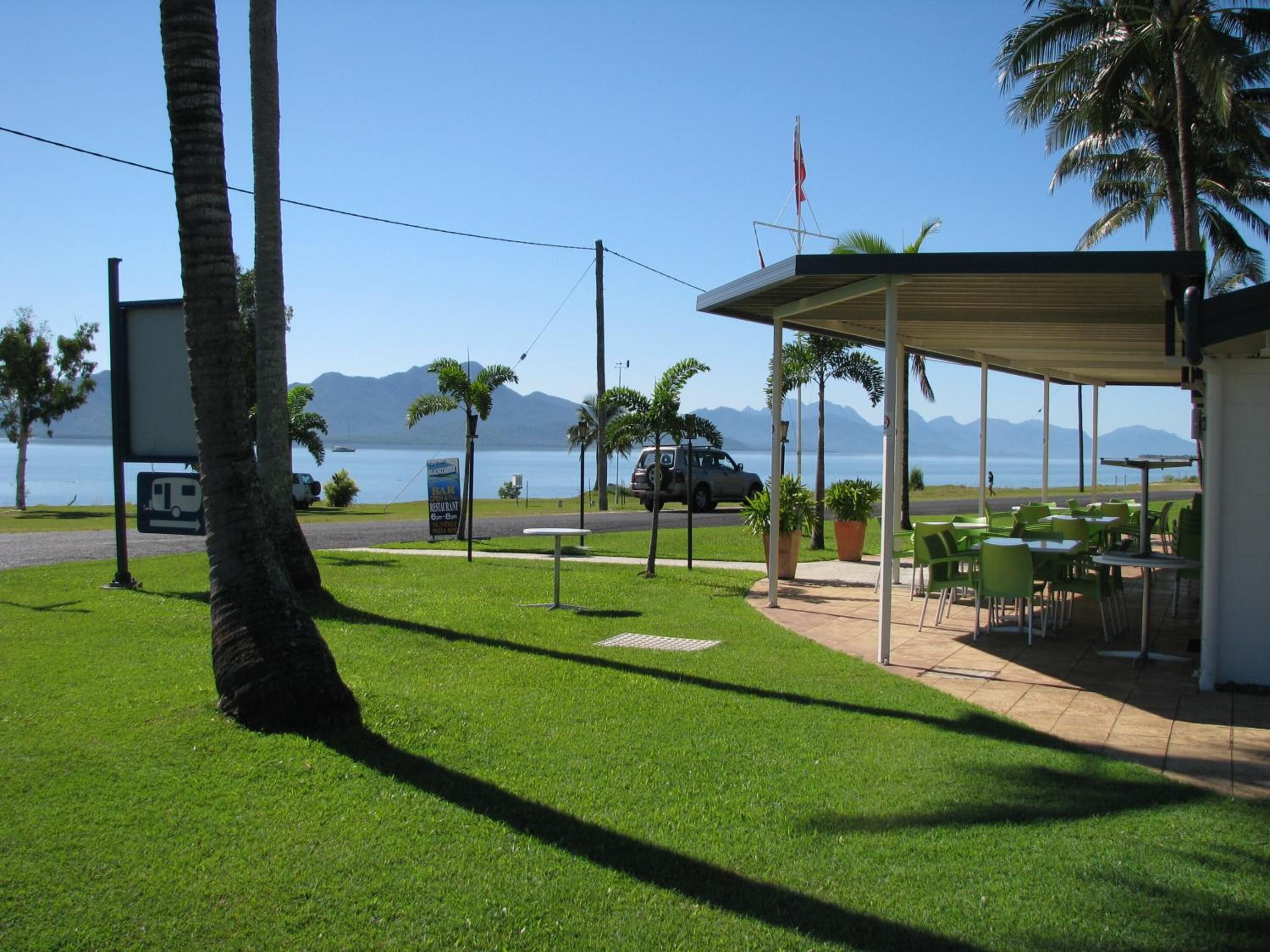 A coastal restaurant with outdoor seating, a view of the sea, and a mountain backdrop.