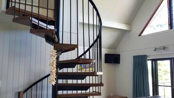 A spacious living area with a curved staircase, a ceiling fan, and a large window providing natural light.
